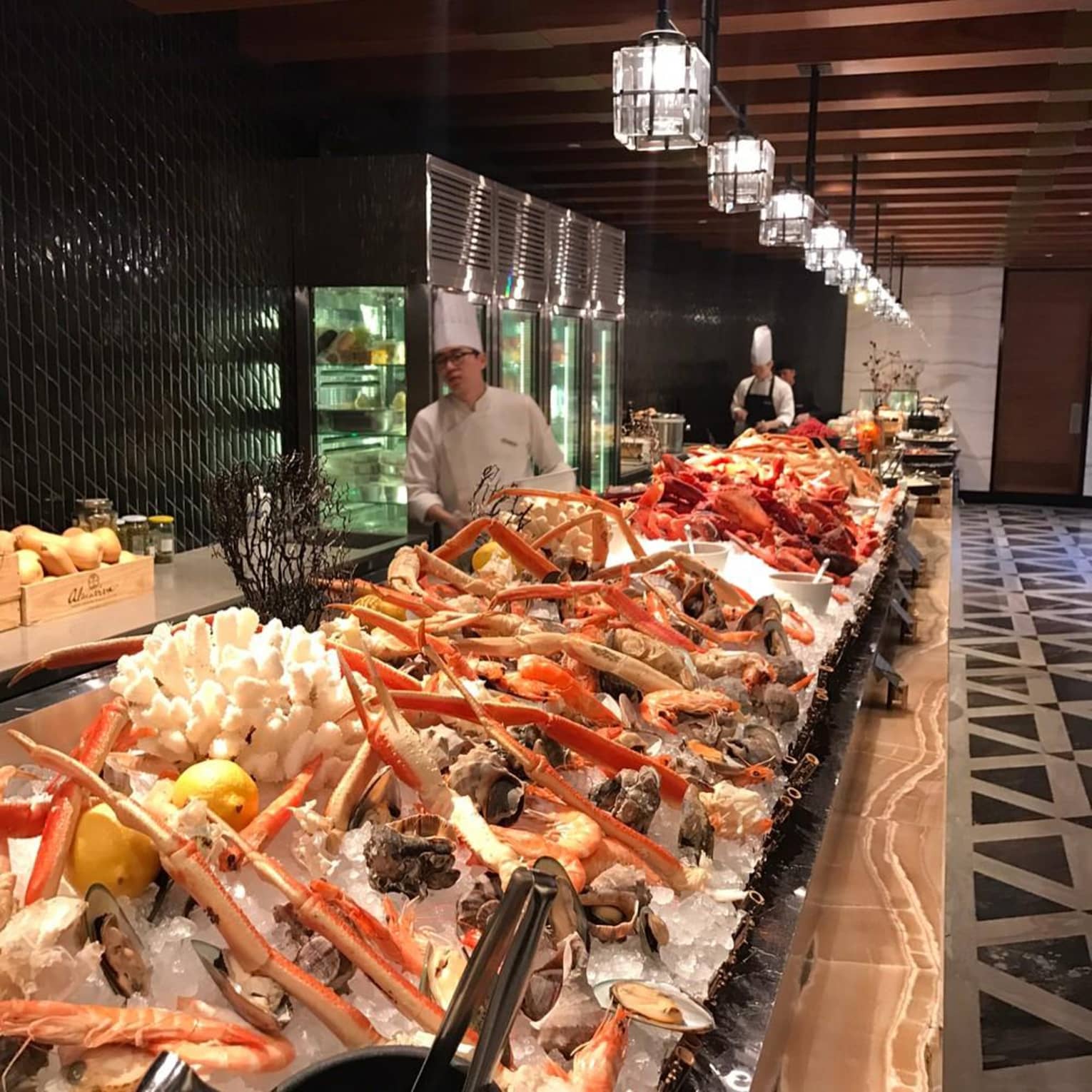 Chef stands behind long seafood buffet with crab legs, oysters on ice
