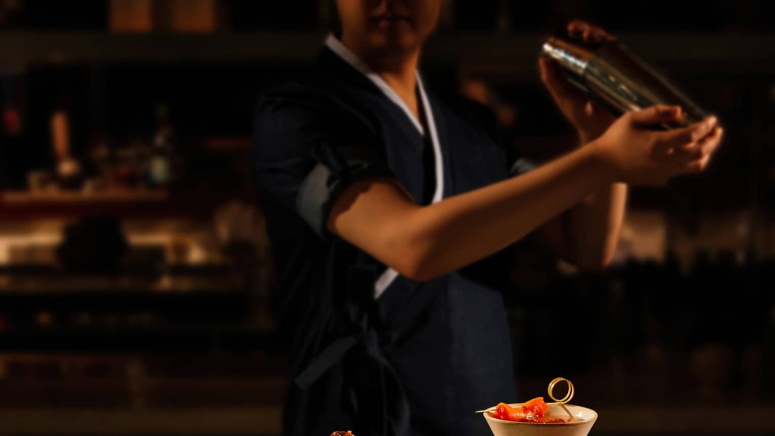 Bartender shaking a cocktail, bar bites at the forefront