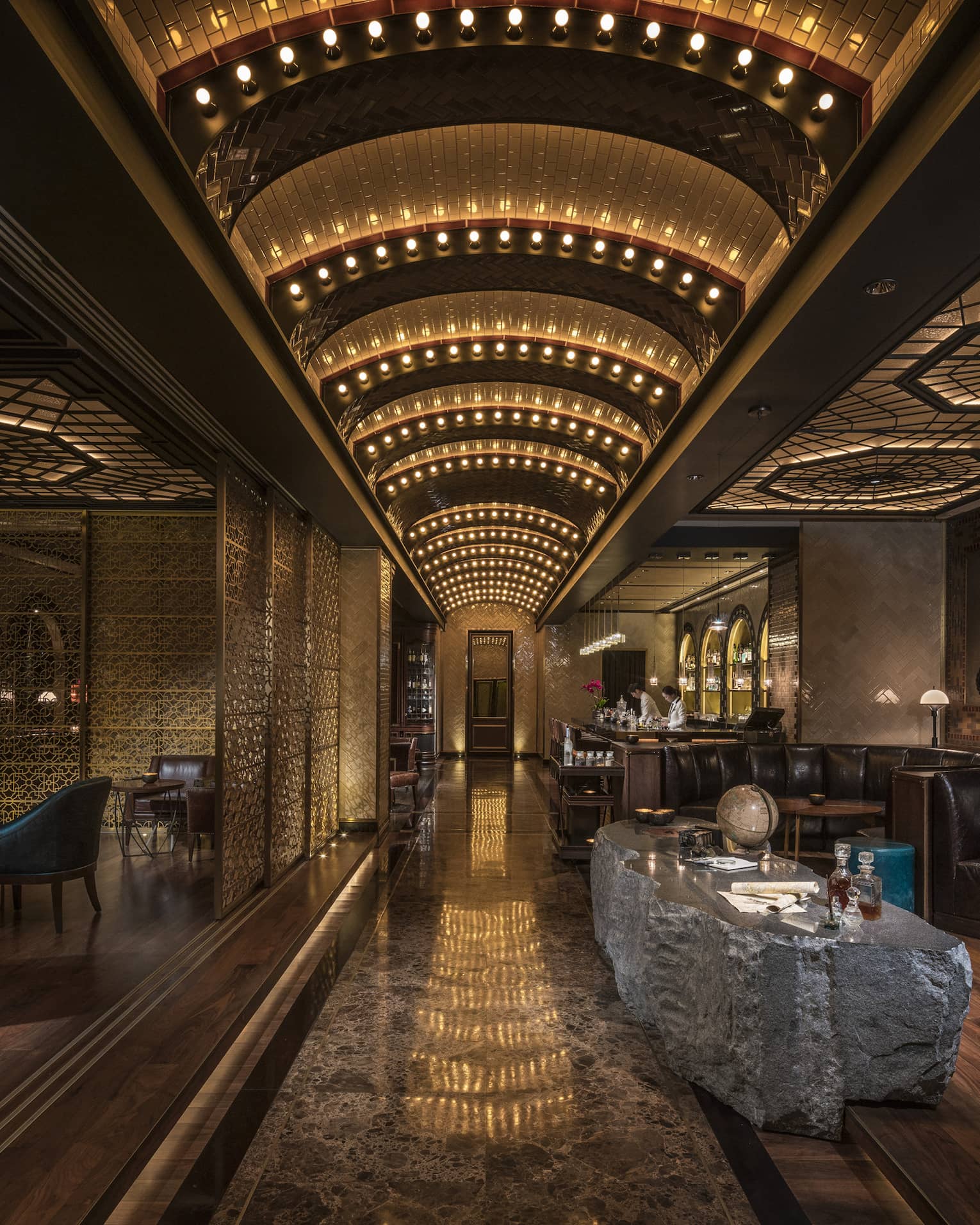 Dimly lit Charles H Bar lounge with stone table, leather banquettes, arched lights 